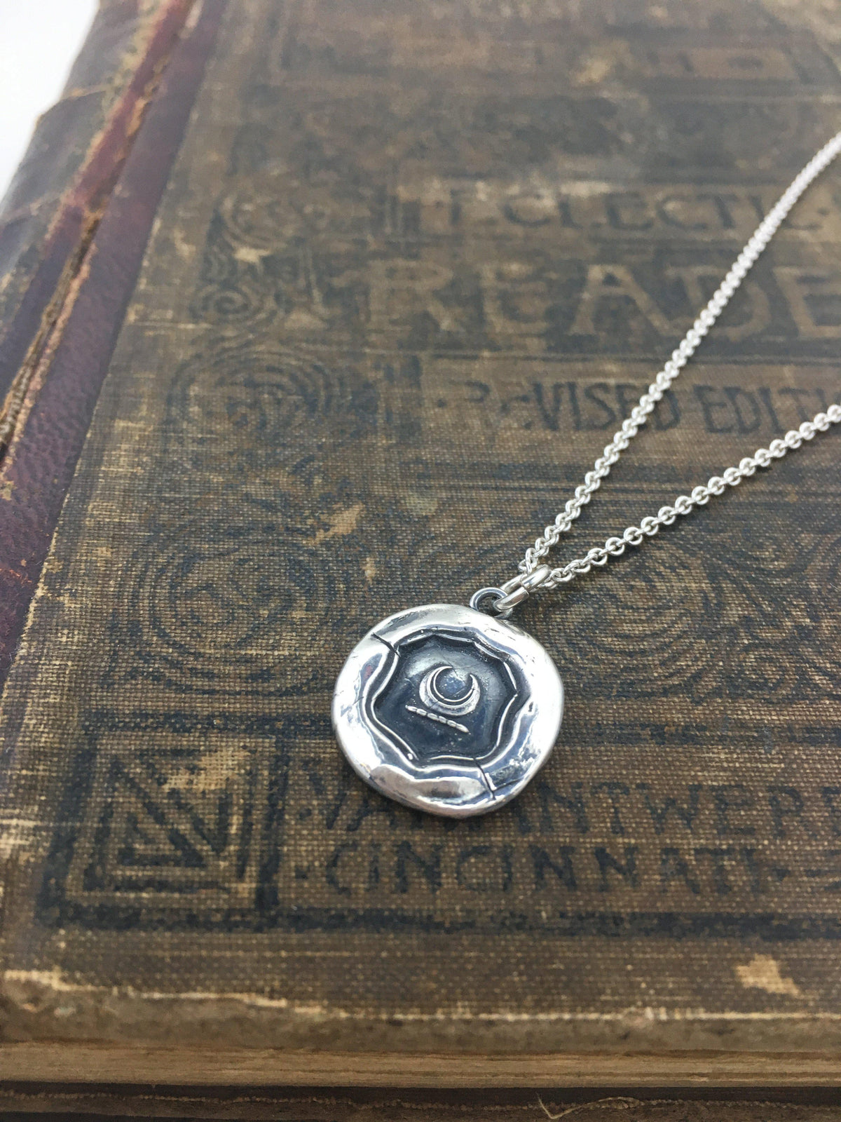 Crescent moon wax seal necklace on a book
