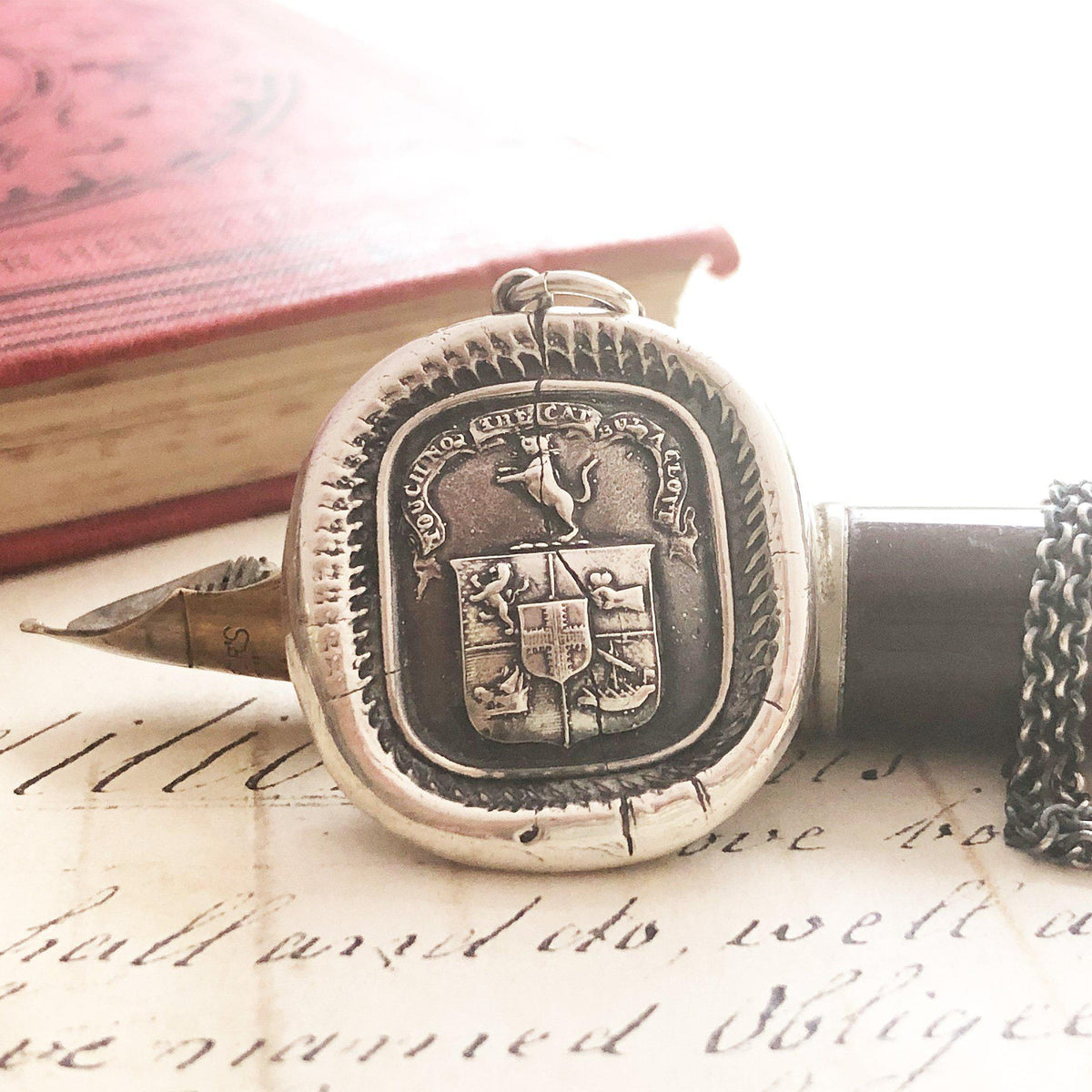 Cat wax seal crest necklace over an old pen