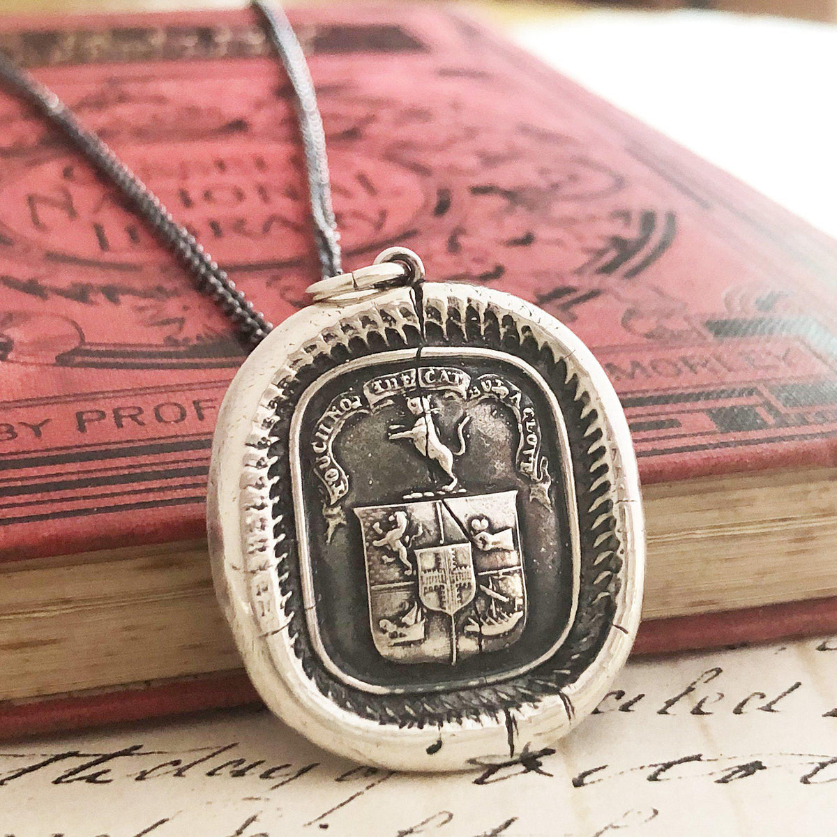 Cat wax seal crest necklace on a book