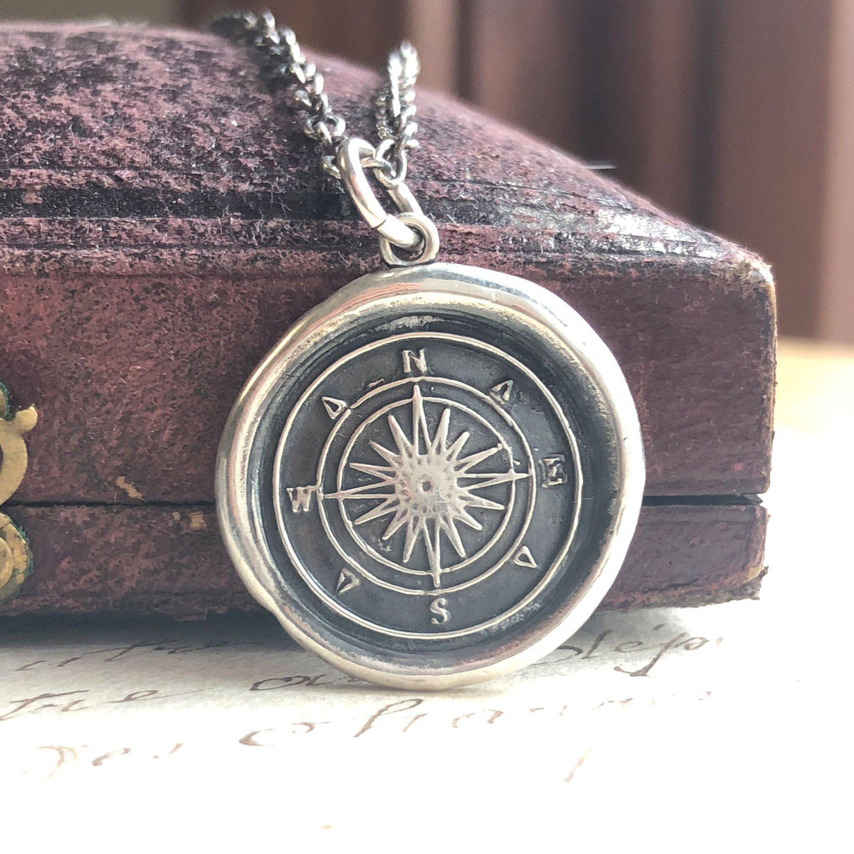 Compass wax seal necklace laying over a book