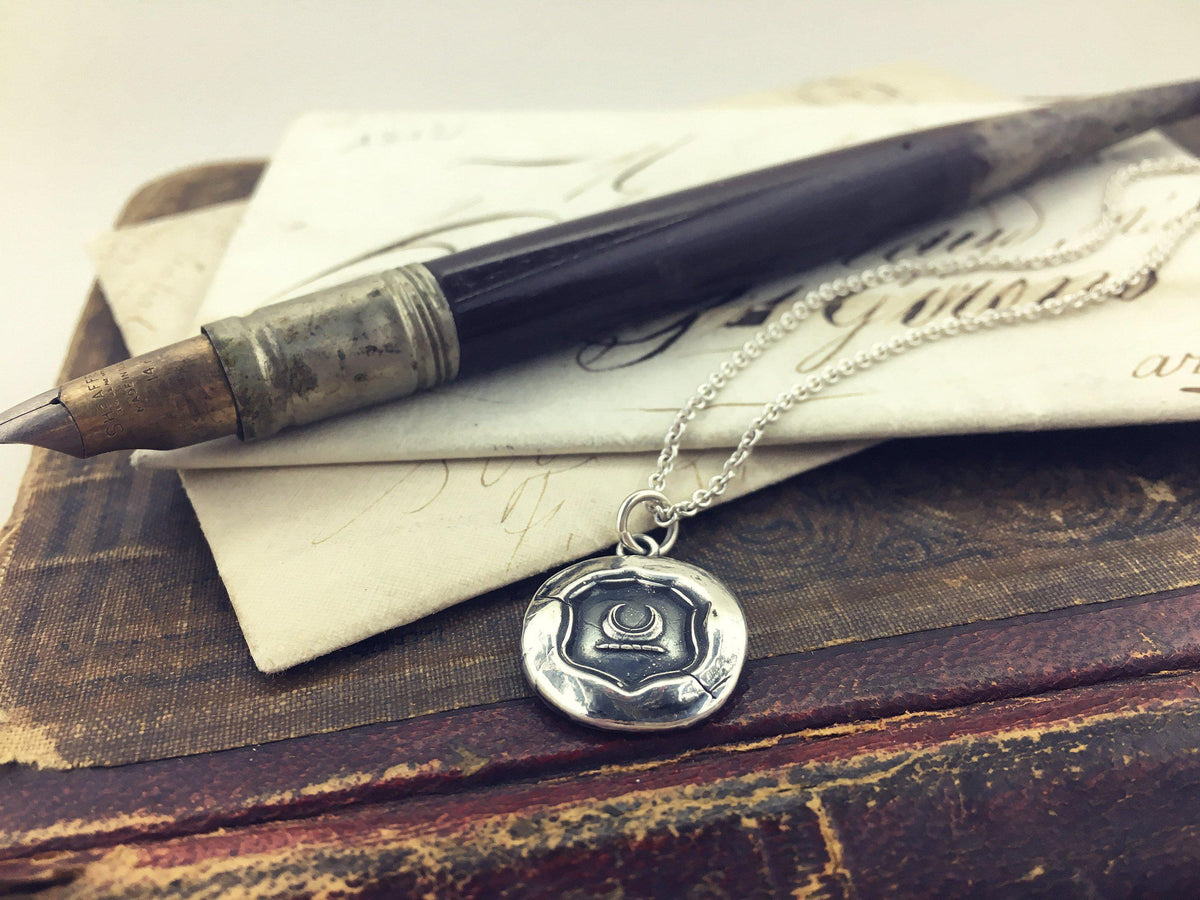 Crescent moon wax seal necklace next to a pen