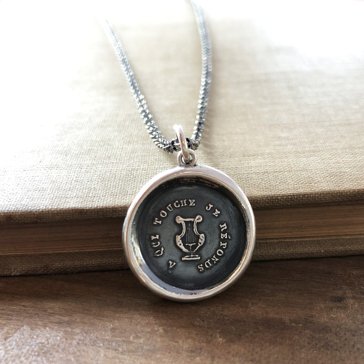 Harp wax seal necklace hung over a book