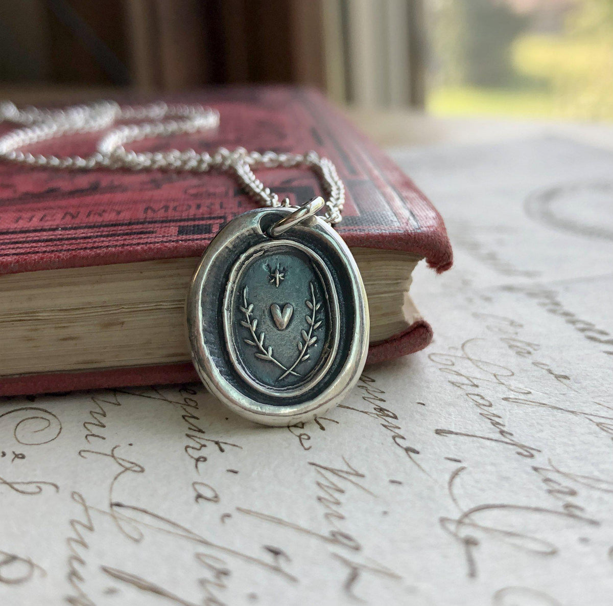 Heart with a star wax seal necklace hung over a book edge
