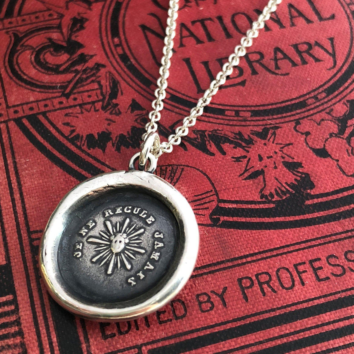 Never back down wax seal necklace on a red book